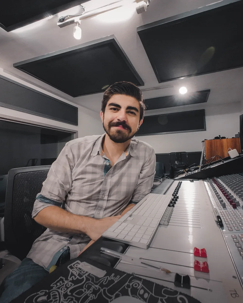 Oliver Mena at the mixing console in the control room, smiling at the camera.